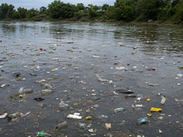 Floating debris and plastic waste in a river before trash boom installation